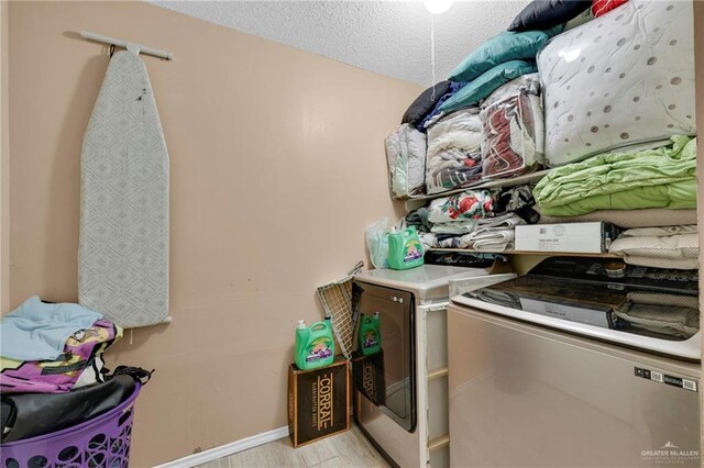 laundry area featuring laundry area, baseboards, a textured ceiling, washer and dryer, and light wood-style floors