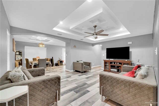 living area featuring light wood-type flooring, arched walkways, a tray ceiling, and baseboards