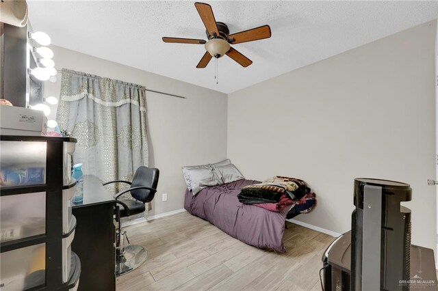 bedroom featuring light wood-style flooring, baseboards, ceiling fan, and a textured ceiling