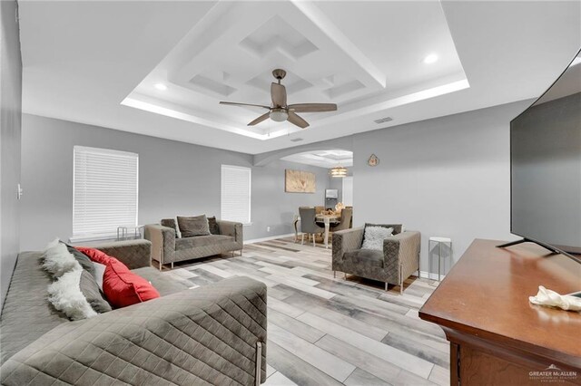 living room with a tray ceiling, arched walkways, ceiling fan, light wood-type flooring, and baseboards