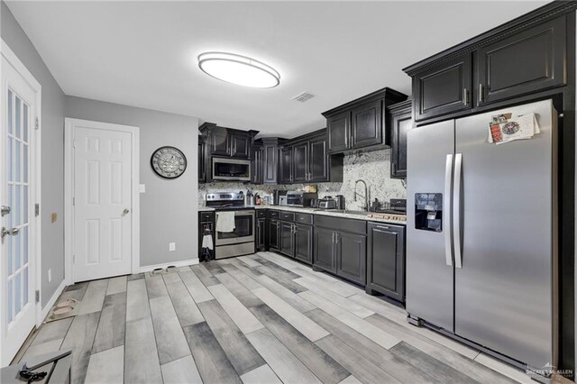 kitchen with stainless steel appliances, light countertops, decorative backsplash, a sink, and dark cabinetry