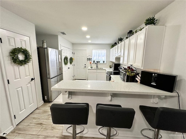 712 Bridget St, Weslaco, TX 78596 - kitchen featuring appliances with stainless steel finishes, a peninsula, light countertops, white cabinetry, and recessed lighting