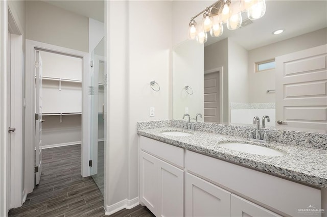 full bath featuring double vanity, a walk in closet, a sink, and wood finished floors