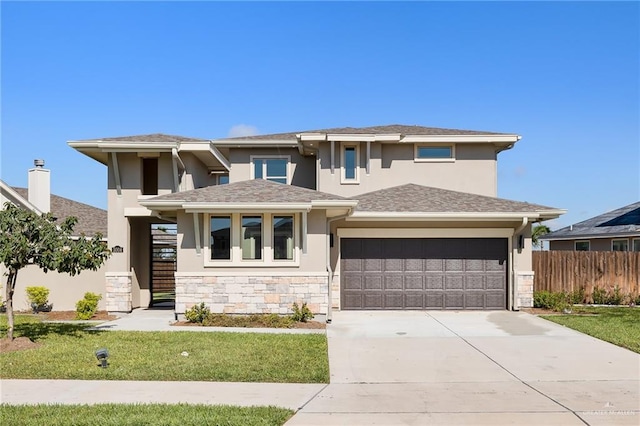 prairie-style home featuring stucco siding, concrete driveway, fence, stone siding, and a front lawn