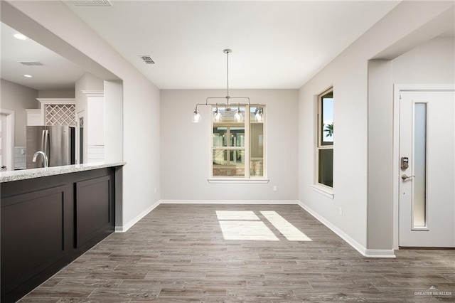 unfurnished dining area featuring an inviting chandelier, wood finished floors, visible vents, and baseboards