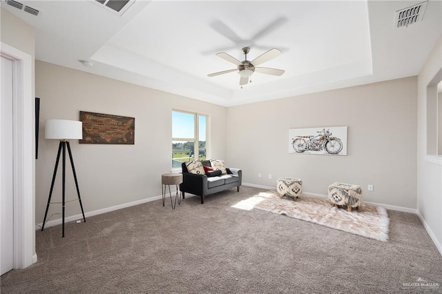 living area with carpet floors, a tray ceiling, visible vents, and baseboards