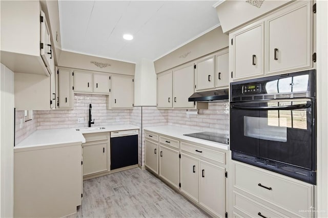 kitchen featuring decorative backsplash, light wood-style floors, a sink, under cabinet range hood, and black appliances