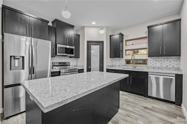 kitchen with a center island, sink, light wood-type flooring, appliances with stainless steel finishes, and decorative light fixtures