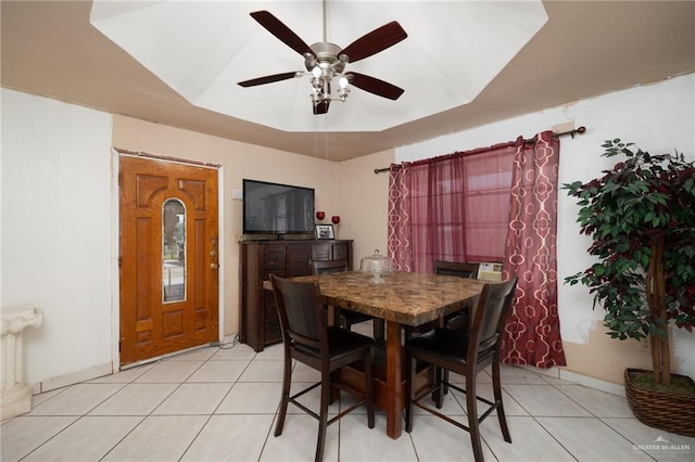 tiled dining space featuring a raised ceiling and ceiling fan