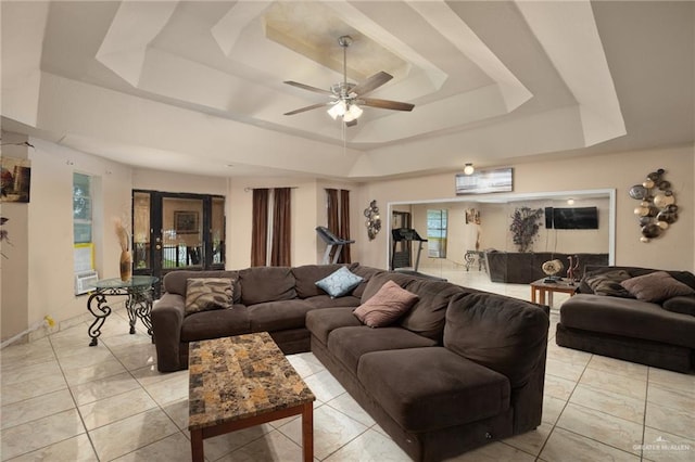 tiled living room with ceiling fan and a tray ceiling