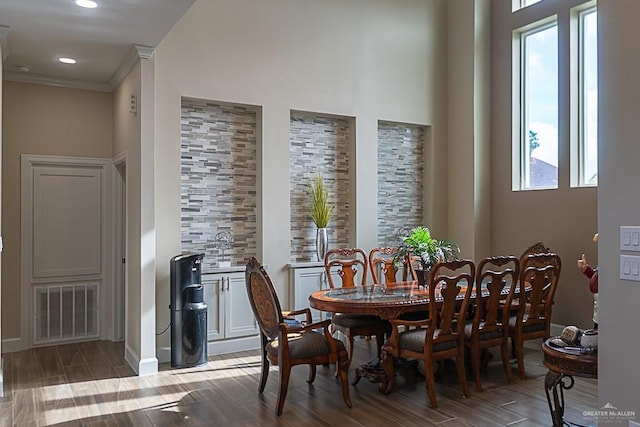 dining area with a towering ceiling, hardwood / wood-style flooring, plenty of natural light, and ornamental molding