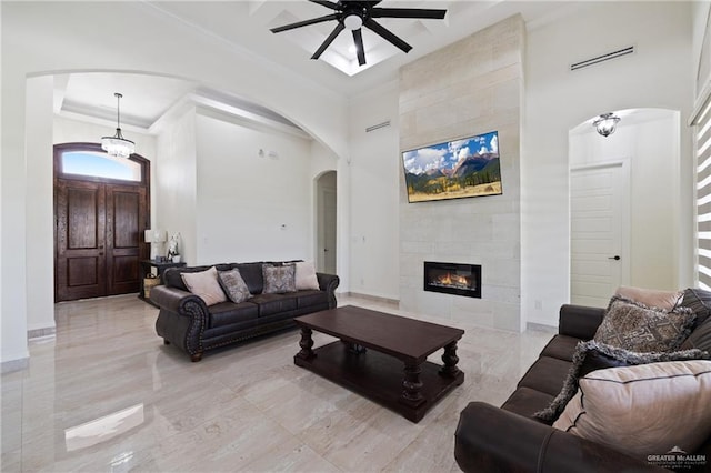 22303 Uresti Rd, Edinburg, TX 78542 - living room with a high ceiling, arched walkways, a ceiling fan, crown molding, and a tile fireplace