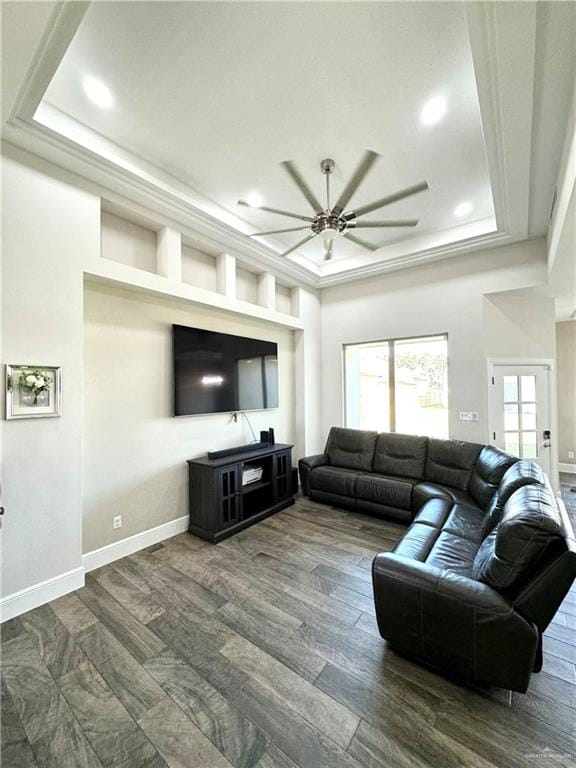 living room with a tray ceiling, ceiling fan, and dark wood-type flooring