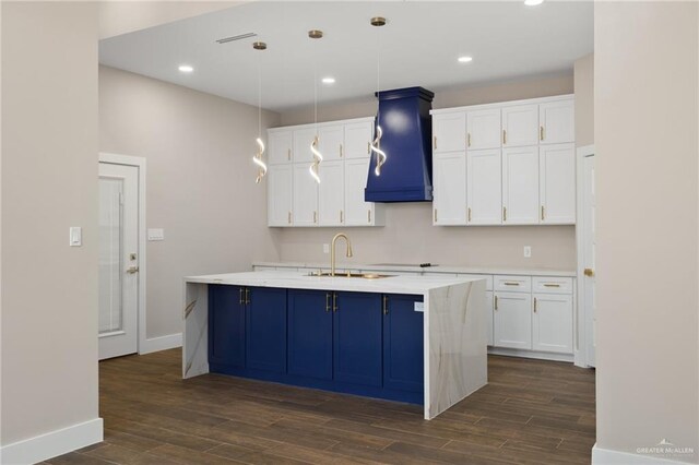 kitchen with white cabinetry, sink, hanging light fixtures, dark hardwood / wood-style flooring, and a center island with sink