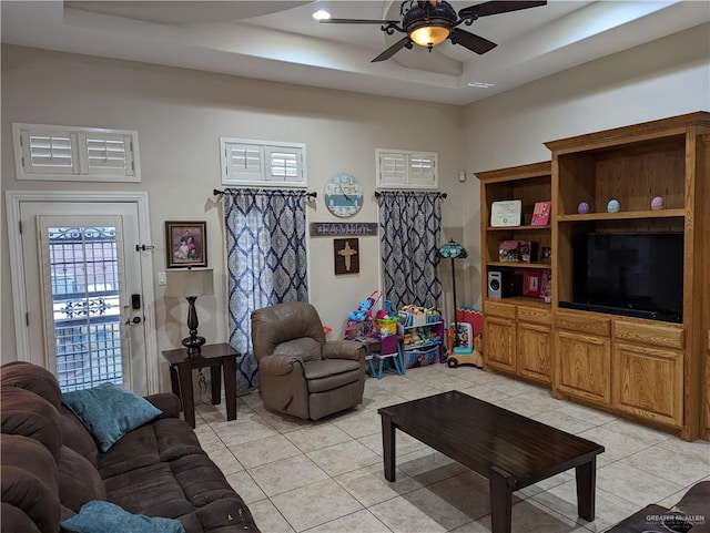 tiled living room with ceiling fan and a tray ceiling