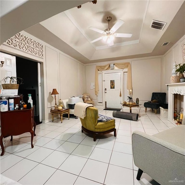 tiled living room featuring a fireplace, a raised ceiling, and ceiling fan