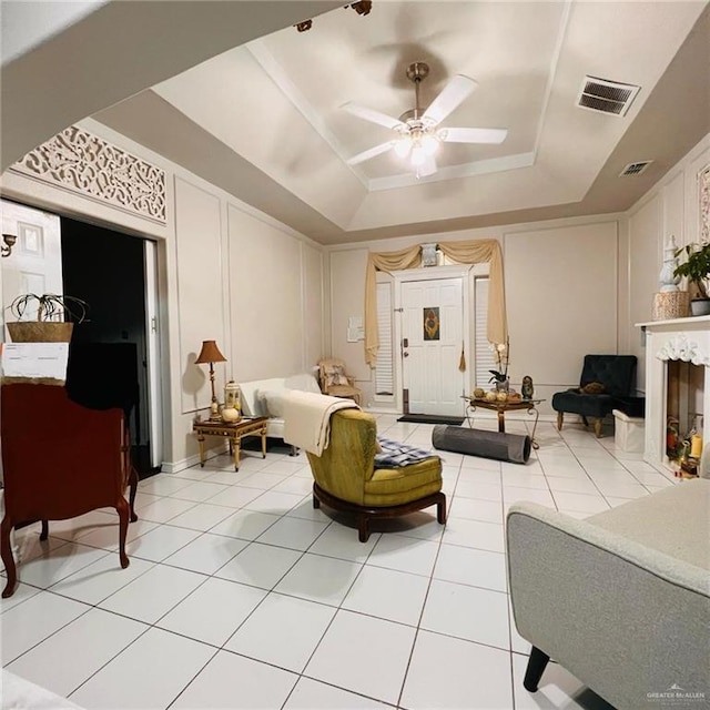 living room featuring ceiling fan, a tray ceiling, tile patterned flooring, and a fireplace