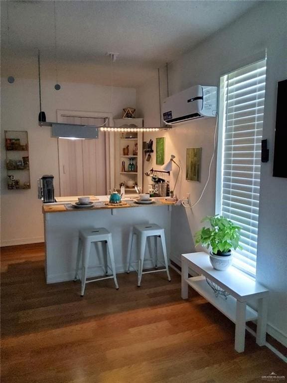 kitchen with a wall mounted air conditioner, a kitchen breakfast bar, kitchen peninsula, and wood-type flooring