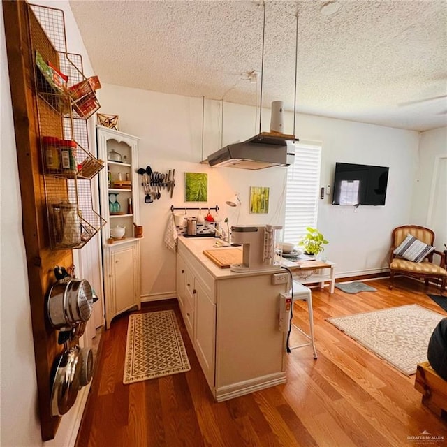 kitchen with island range hood, light hardwood / wood-style flooring, a textured ceiling, and a kitchen bar