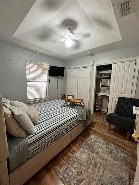 bedroom with dark hardwood / wood-style flooring, two closets, a textured ceiling, and ceiling fan