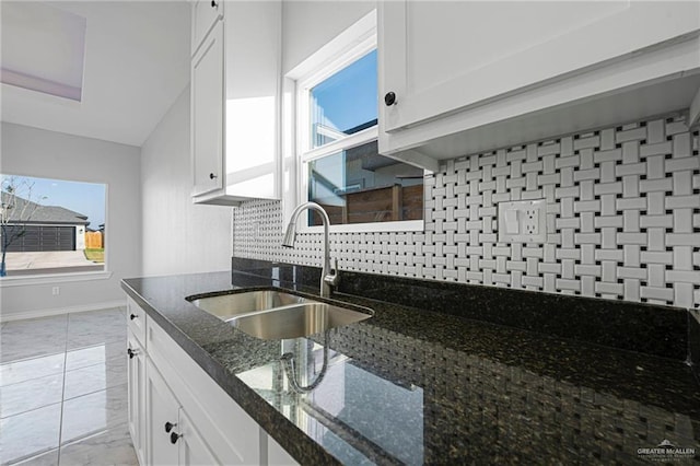 kitchen featuring backsplash, sink, dark stone countertops, a healthy amount of sunlight, and white cabinetry