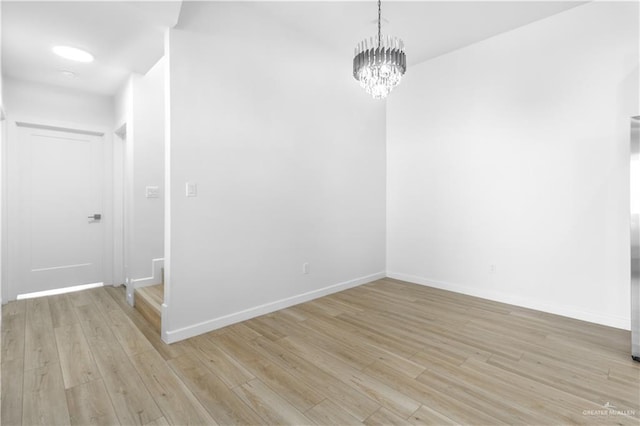 empty room with a notable chandelier and light hardwood / wood-style floors