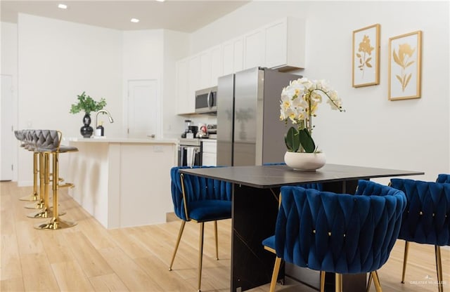 kitchen with kitchen peninsula, a breakfast bar, stainless steel appliances, light hardwood / wood-style floors, and white cabinetry