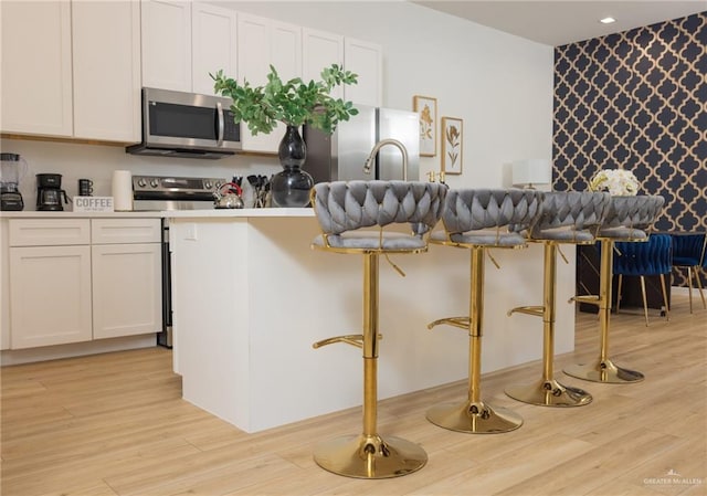 kitchen with a breakfast bar area, white cabinets, light wood-type flooring, and appliances with stainless steel finishes