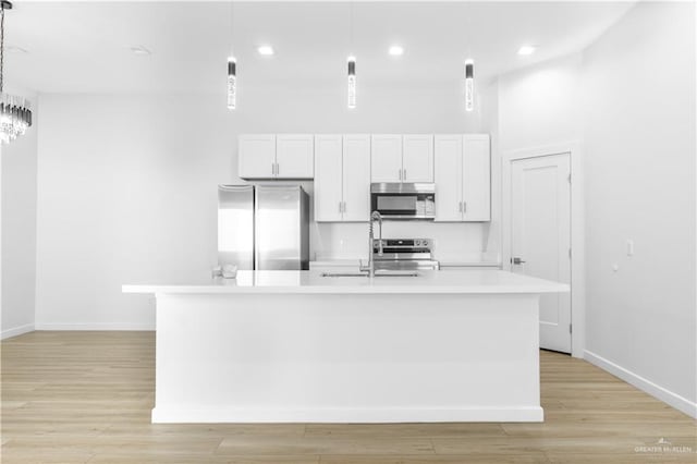 kitchen with pendant lighting, light hardwood / wood-style flooring, an island with sink, white cabinetry, and stainless steel appliances