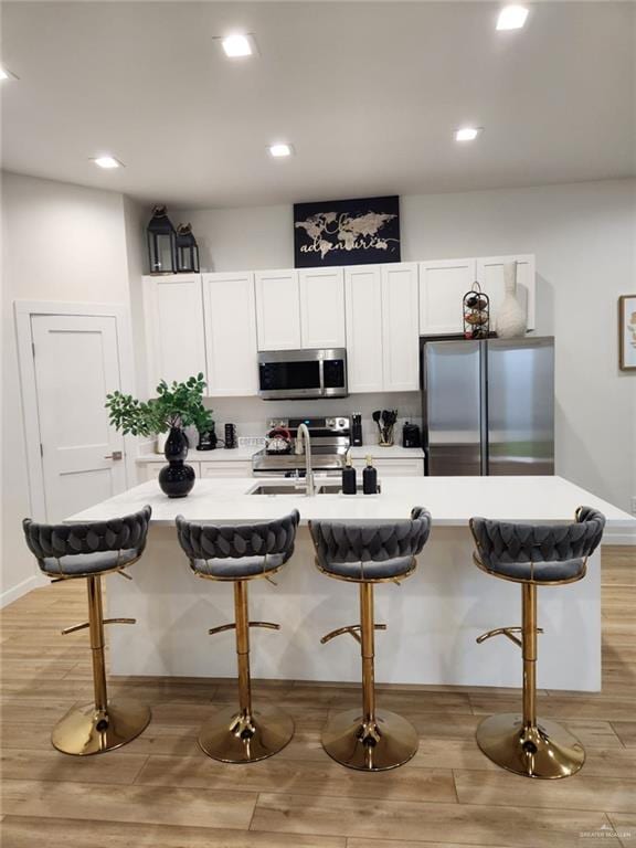 kitchen with white cabinetry, stainless steel appliances, an island with sink, a breakfast bar area, and light wood-type flooring