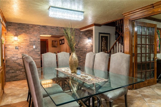 tiled dining space with brick wall, a textured ceiling, and ornamental molding