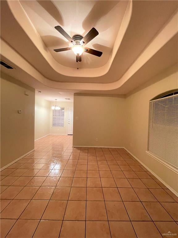 tiled empty room with a tray ceiling and ceiling fan with notable chandelier