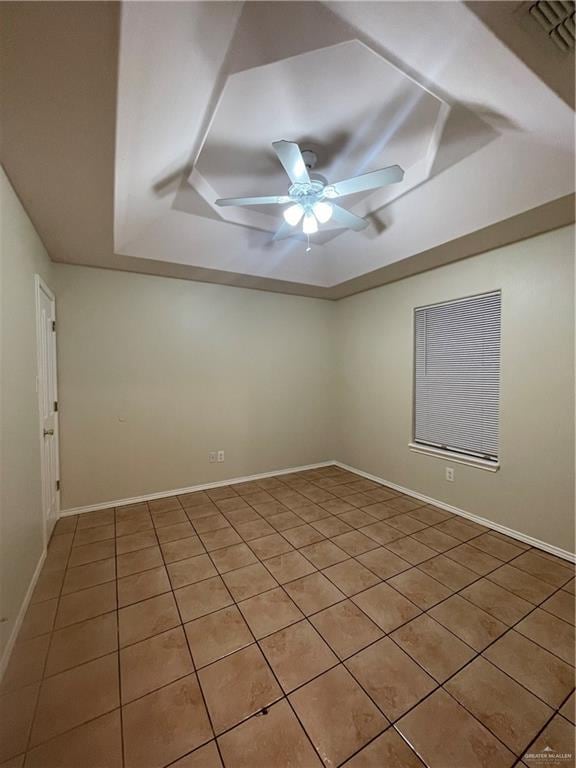 empty room with a raised ceiling, ceiling fan, and light tile patterned flooring