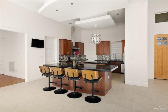 kitchen featuring a high ceiling, a kitchen island, decorative backsplash, and wall chimney exhaust hood