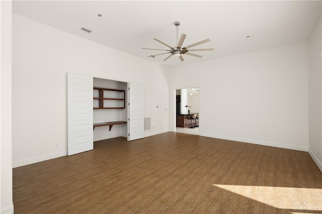 unfurnished room with dark wood-type flooring, built in desk, and ceiling fan