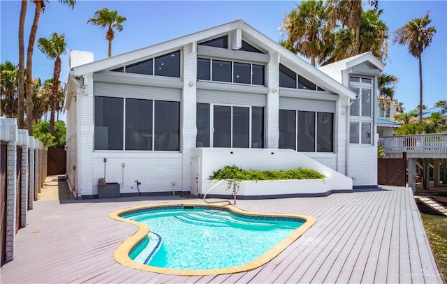 rear view of property with a sunroom, a pool side deck, and a patio