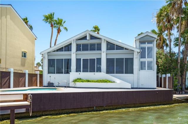 back of house with a water view, a fenced in pool, and a sunroom