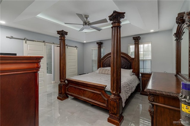 bedroom with ceiling fan, a barn door, and a raised ceiling