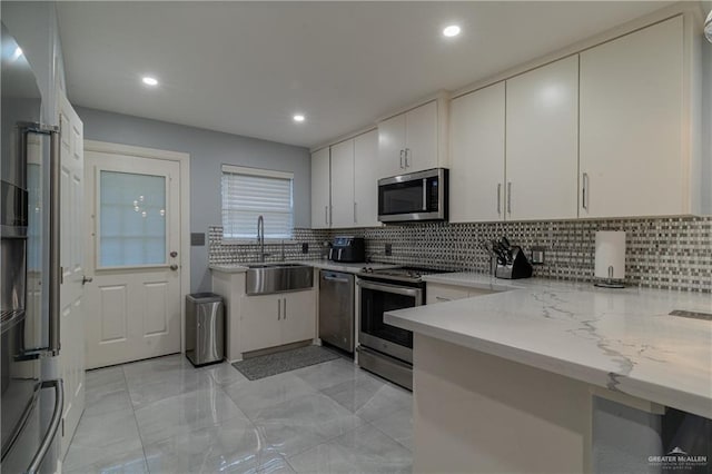 kitchen with tasteful backsplash, sink, appliances with stainless steel finishes, white cabinets, and light stone counters