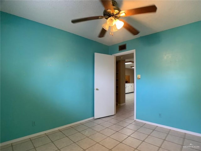 empty room featuring light tile patterned floors, visible vents, baseboards, and a ceiling fan