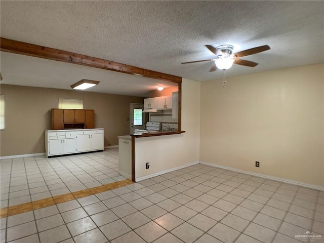 kitchen featuring baseboards, white range with electric cooktop, beam ceiling, light tile patterned flooring, and a textured ceiling