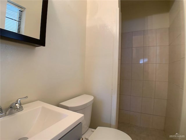 full bathroom featuring tiled shower, toilet, and vanity