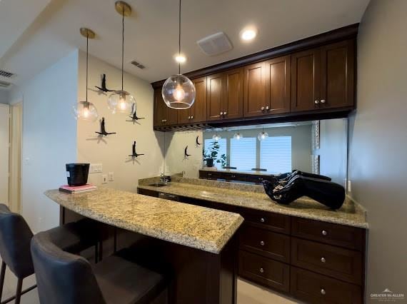 kitchen with a kitchen bar, dark brown cabinetry, light stone countertops, and decorative light fixtures