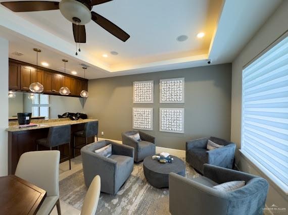 living room with ceiling fan, a raised ceiling, and a wealth of natural light