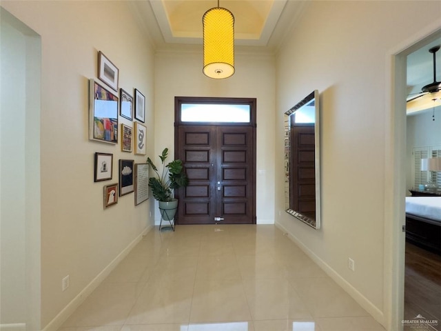 tiled foyer featuring a tray ceiling, ceiling fan, and crown molding