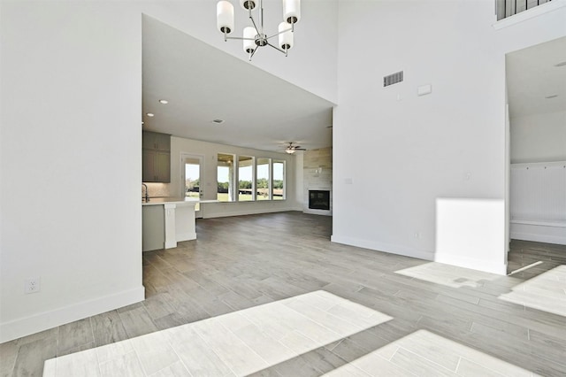 living room featuring ceiling fan with notable chandelier, light wood-type flooring, and a high ceiling