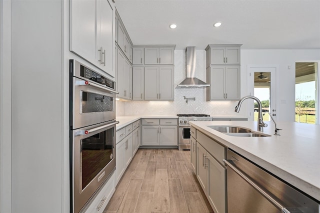 kitchen featuring appliances with stainless steel finishes, wall chimney exhaust hood, backsplash, light wood-type flooring, and sink