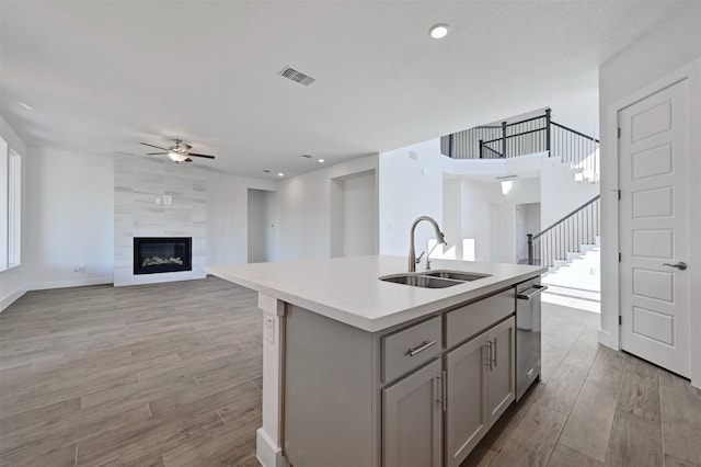 kitchen with a tile fireplace, gray cabinets, tile walls, a kitchen island with sink, and sink