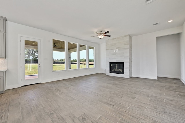 unfurnished living room featuring tile walls, a fireplace, ceiling fan, and light hardwood / wood-style flooring