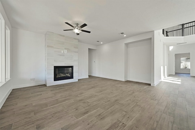 unfurnished living room featuring a tiled fireplace, ceiling fan, tile walls, and light hardwood / wood-style flooring